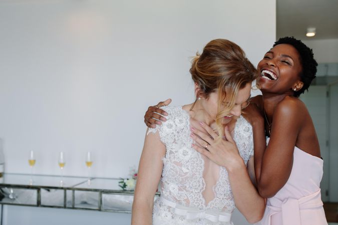 Happy gorgeous bride in white dress having fun with bridesmaid