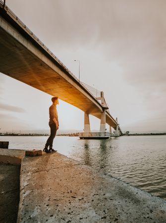 Man standing under bridge beside body of water during golden hours