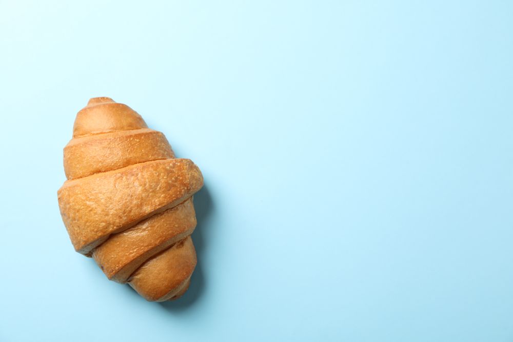 Freshly baked croissant on blue background, top view, copy space