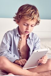 Serious boy using tablet on bed
