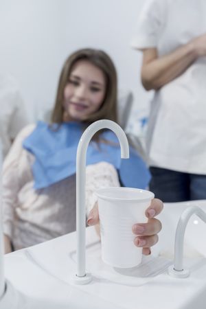 Patient in dentist office taking a cup of water after treatment