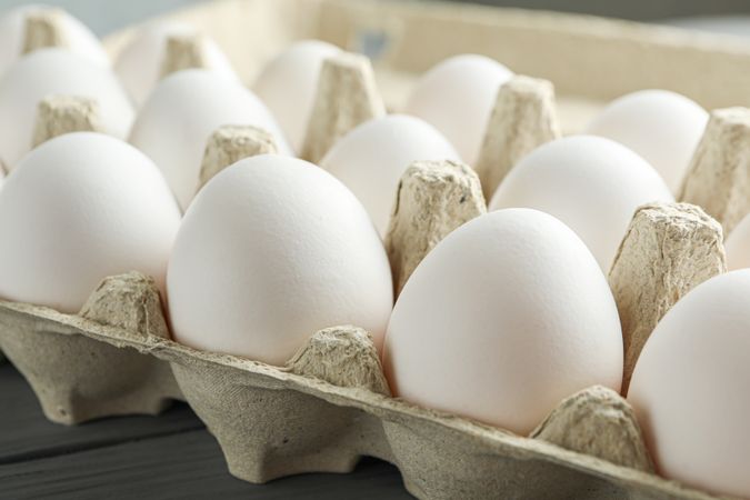 chicken eggs in carton box on wooden table, space for text and closeup