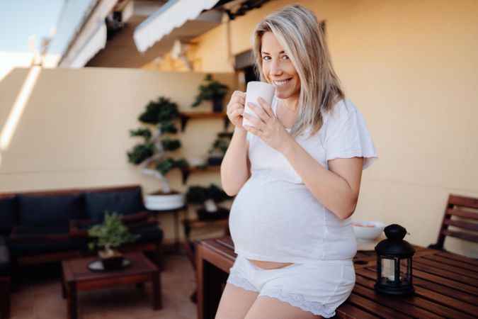 Smiling pregnant woman having drink at terrace