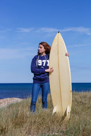 Woman with surfboard in seaside with dry vegetation