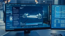Professional Engineer Works on a Computer with a 3D CAD Software and Tests the Electric Car Chassis Prototype with Wheels, Batteries and Engine Standing in a High Tech Development Laboratory.