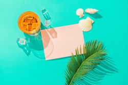 Cocktail with ice cubes, palm leaf, sea shells and pink paper card note on vivid blue background