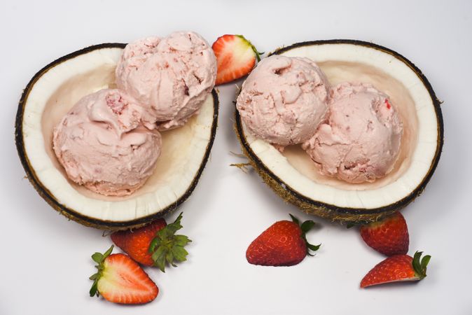 Top view of two coconut shells with ice cream and pieces of strawberry fruit