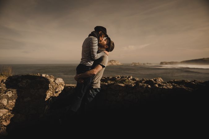 Man kissing and holding woman on hands near stones on shore