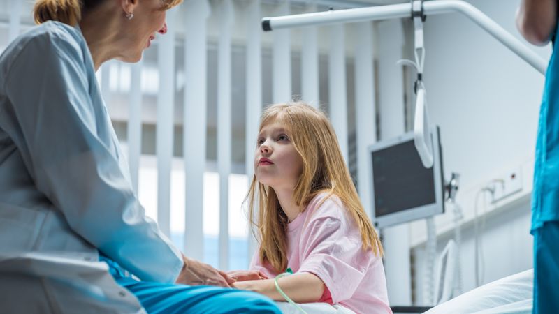 Recovering Little Girl Sits on a Hospital Bed and Talks with Friendly Woman Doctor