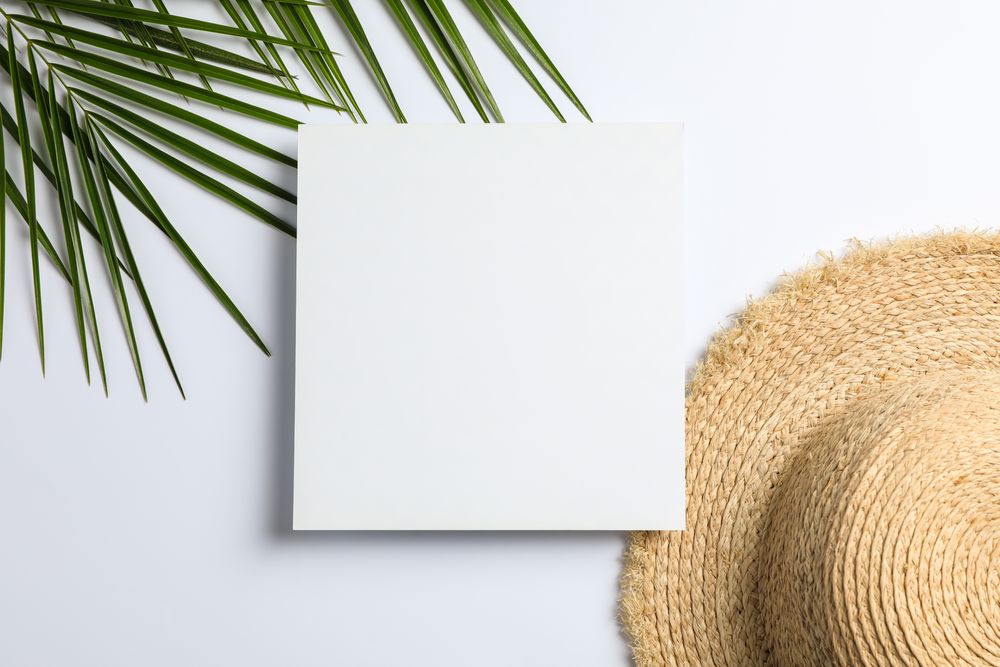 Square with space for text, palm leaves and straw hat on plain background, top view
