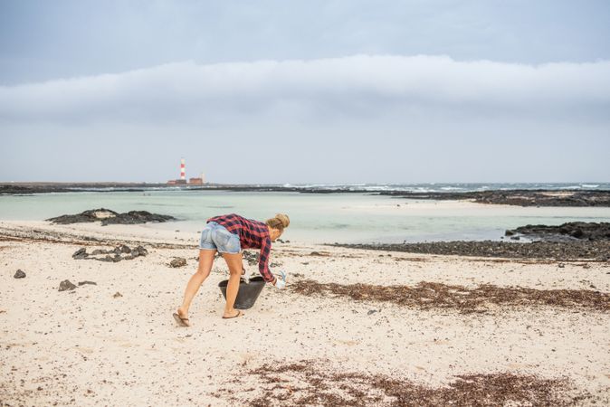 Content modern woman picking litter from sandy seashore