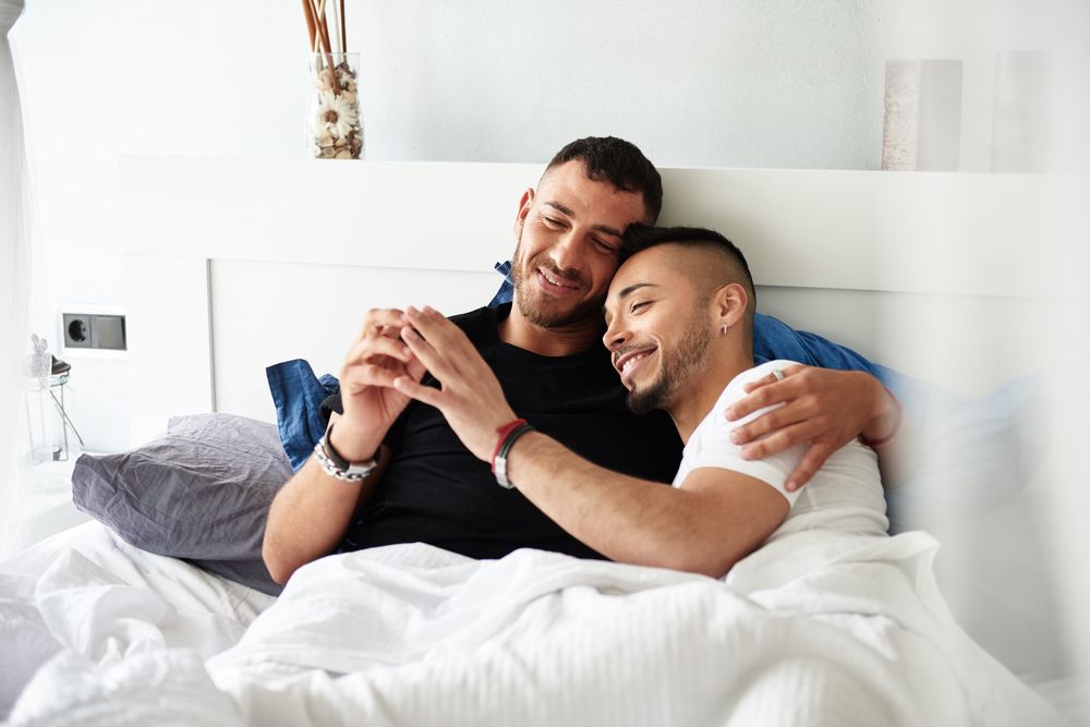 Smiling gay couple hugging on bed