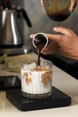 Pouring Coffee Espresso Chocolate using Measuring Cup to the Glass with Fresh Milk