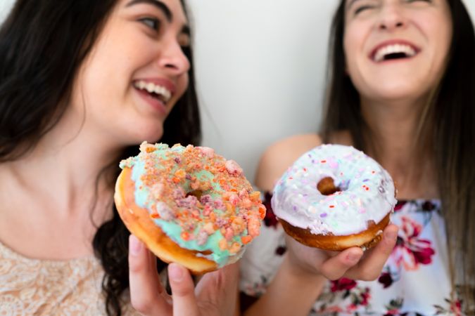 Joyful female friends eating donuts at wall