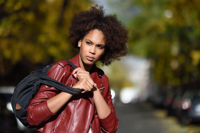 Woman looking away in red leather jacket standing in sunny road