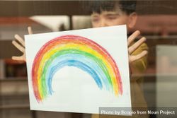 Boy showing rainbow drawing from window glass 4OZoE5