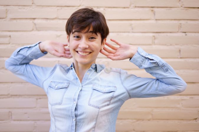 A Cheerful Young Woman with Short Hair Posing in Front of a Stylish Brick Wall Backdrop
