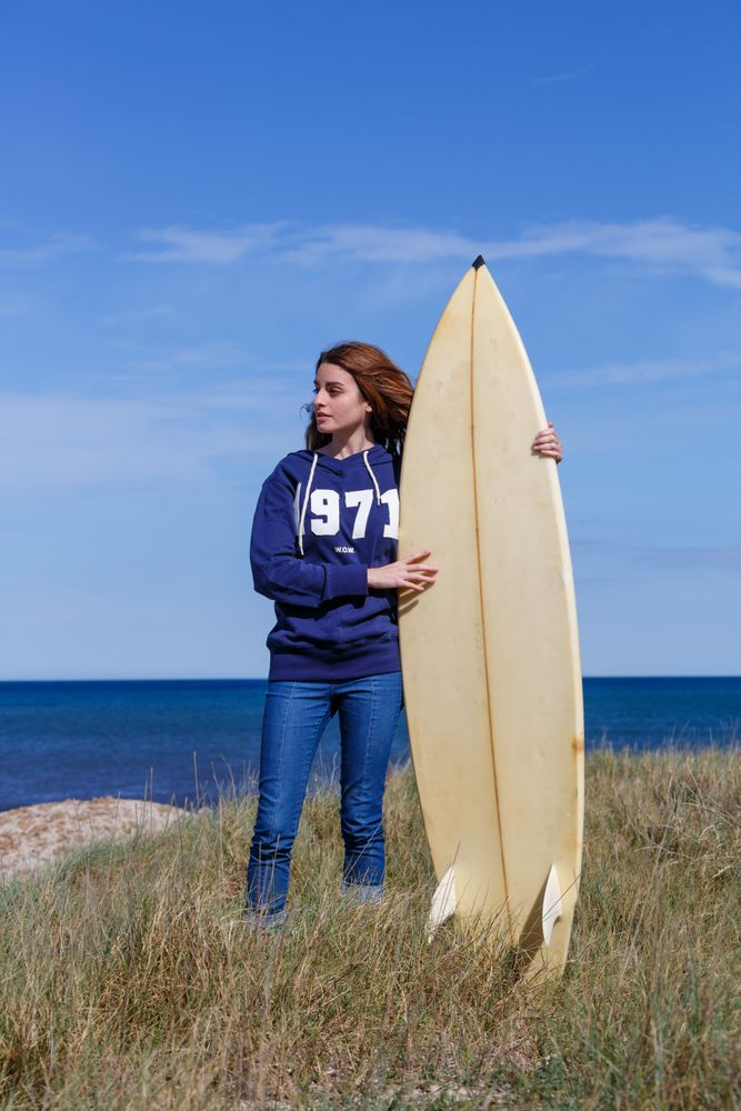 Woman with surfboard in seaside with dry vegetation