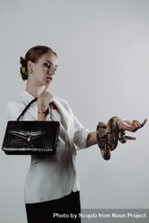 Woman holding dark leather bag with one hand and snake with the other hand 5qLQa0