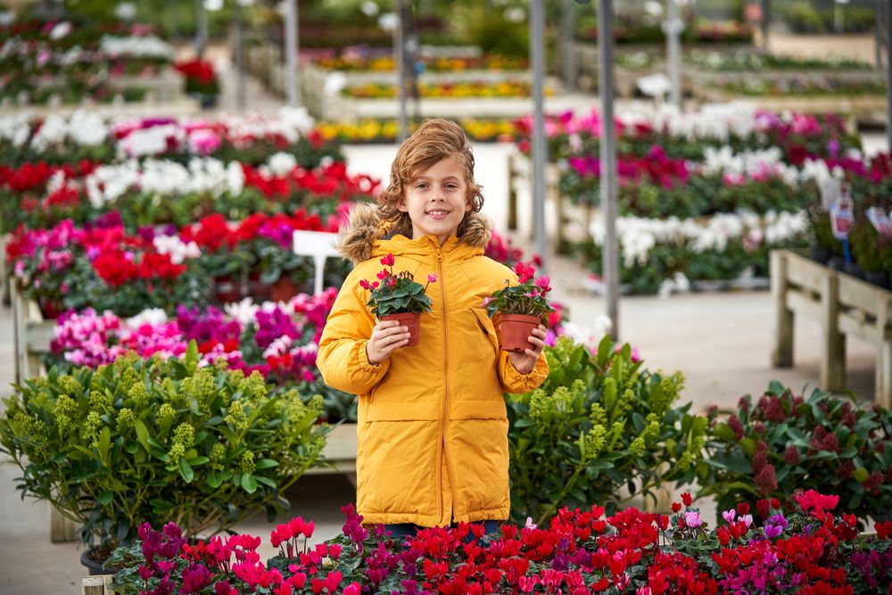 Cheerful preteen boy with blooming potted flowers in garden