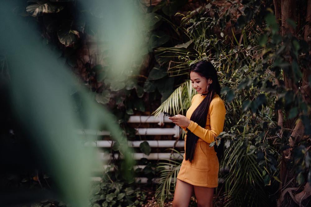 Charming long haired Asian woman browsing smartphone in botanical garden