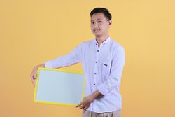 Portrait a young man in yellow backdrop holding a blank note board