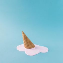Melted pink ice cream and waffle cone on pastel blue background