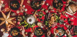 Group of people at festive red table with cake, roast chicken, decorations