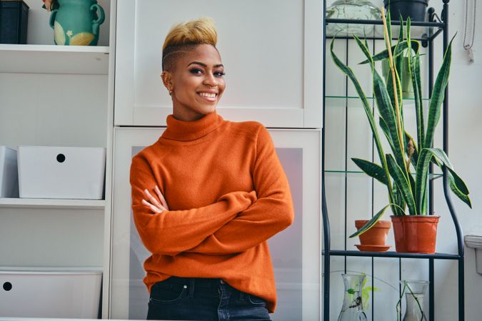 Smiling Black woman with arms crossed in a bright home with plants
