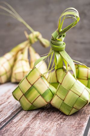Uncooked ketupat filled with rice, placed on wooden surface
