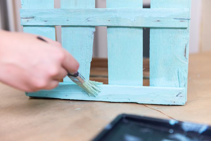 Woman paining wooden box in blue color with brush