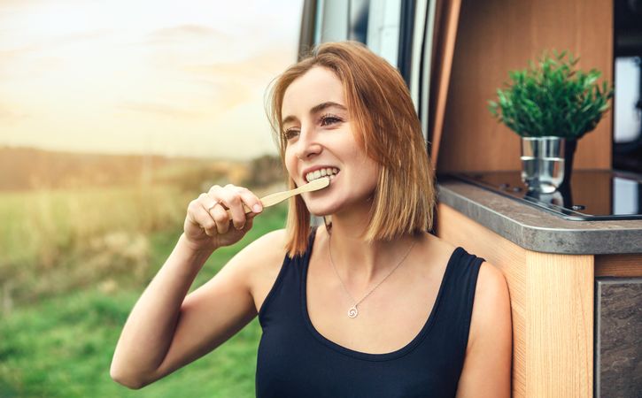 Female on road trip brushing teeth outside of van