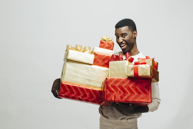 Black man making funny face holding pile of wrapped presents in both arms as glitter falls