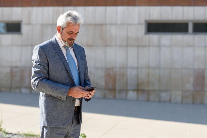 Older male in formal suit checking his phone outside