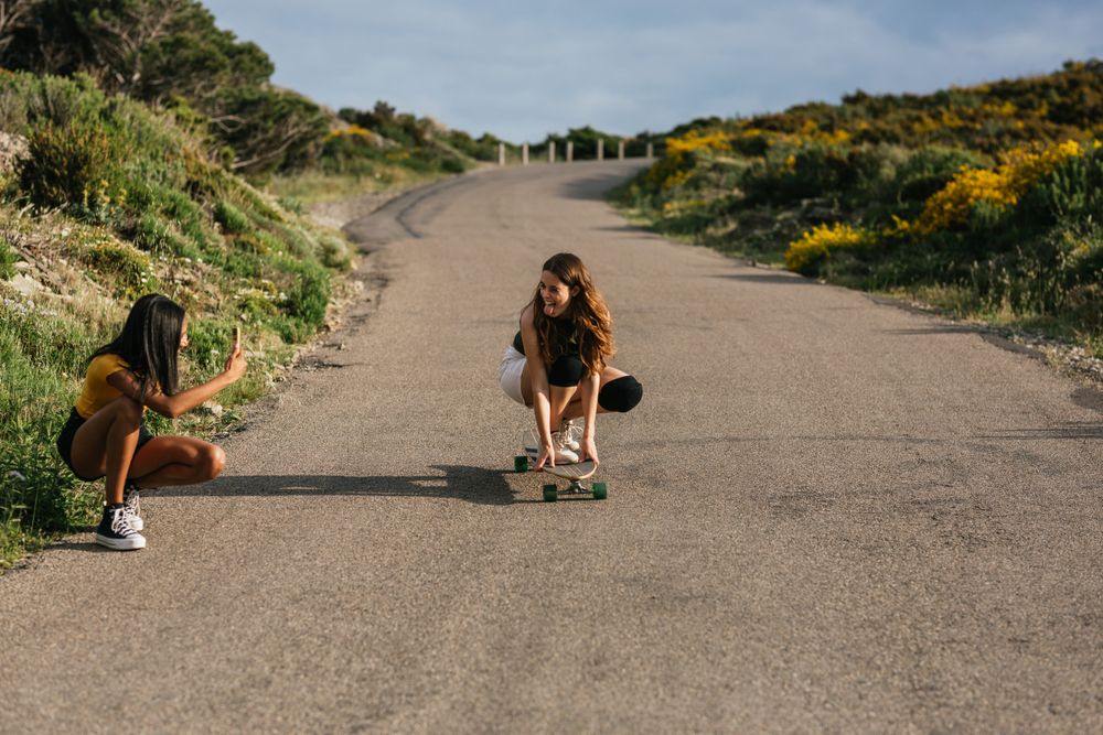 Latina woman taking photo of friend balancing on longboard