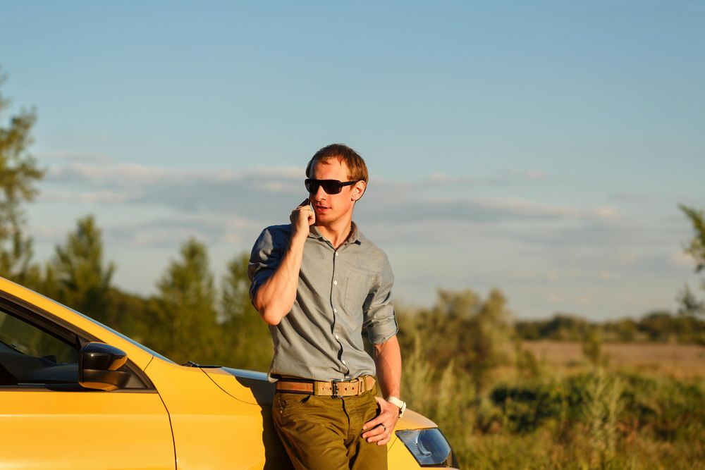 Male talking on his cell phone while leaning on side of stopped yellow car late afternoon