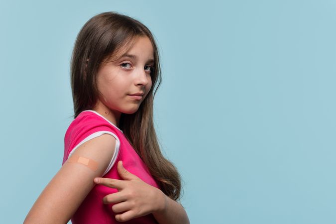 Girl proudly pointing at bandage after receiving vaccination