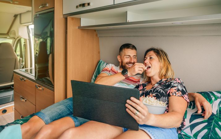 Male and female eating popcorn and watching a movie on a motorhome bed