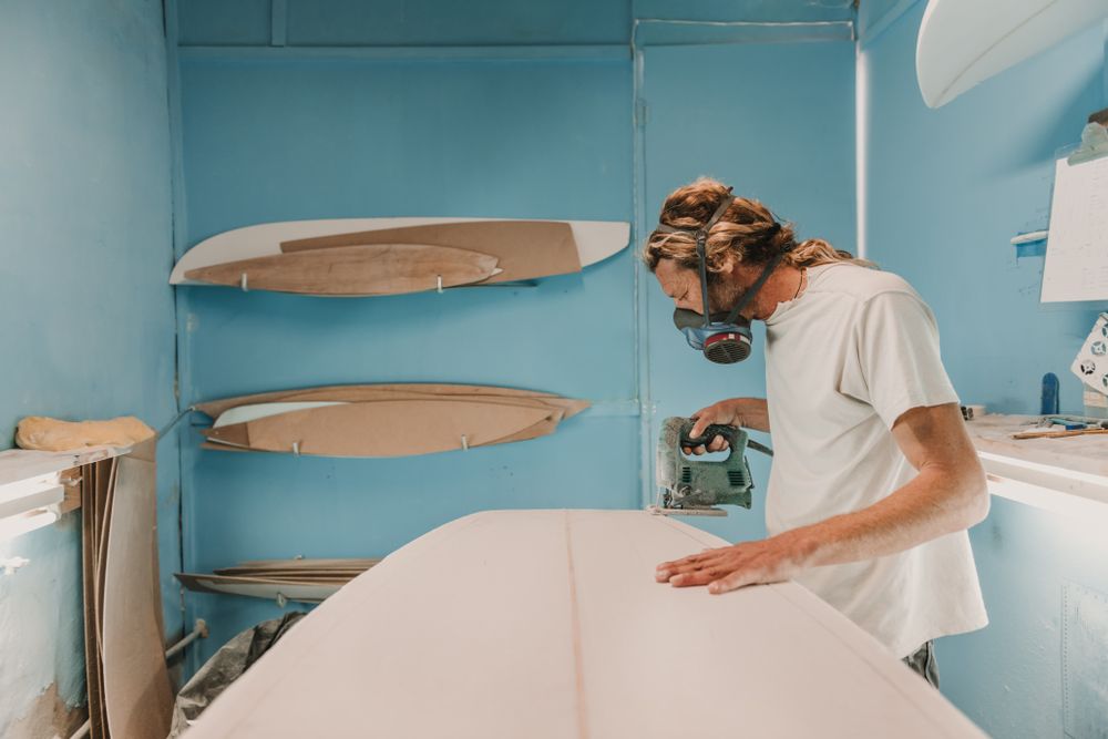 Man with tool sawing surf board in workshop