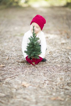 Girl In Red Mittens and Cap Near Small Christmas Tree