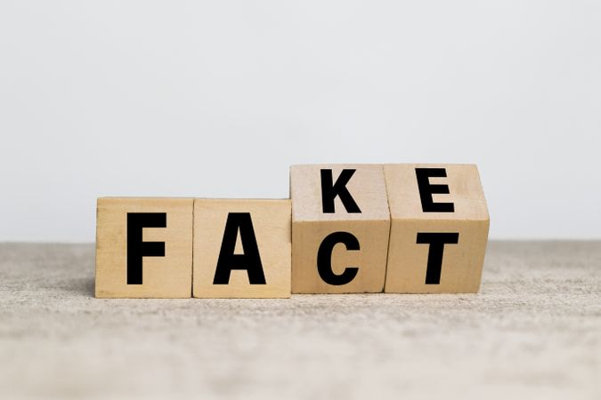 flip wooden blocks with fake and fact words symbol on neutral background
