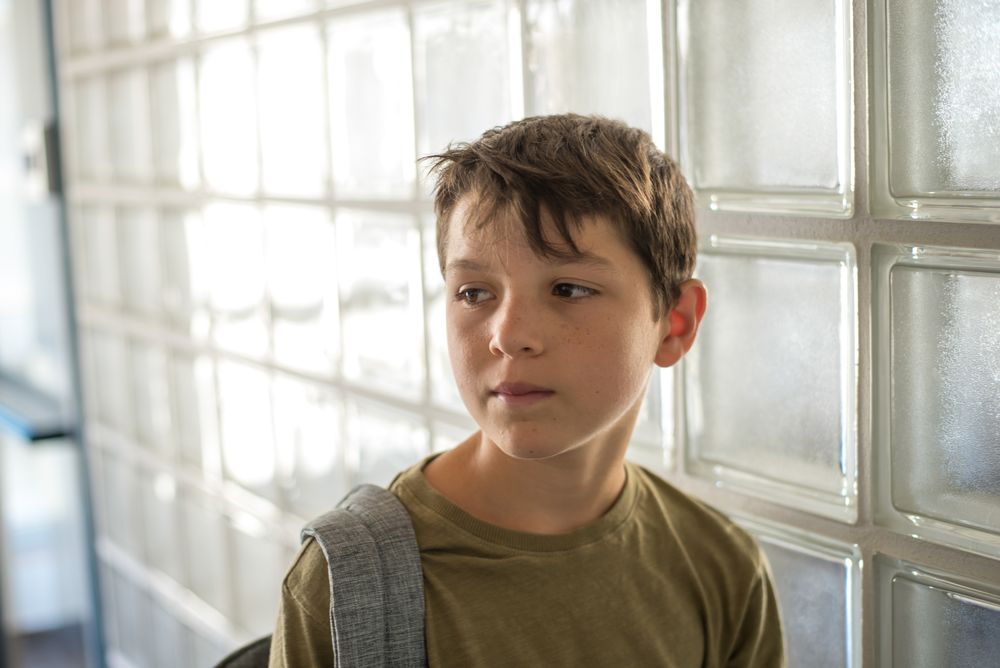 Sad teenager standing with backpack in school