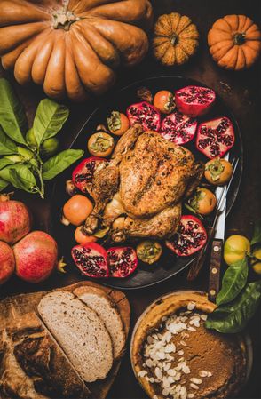 Roasted chicken on table with pomegranates, squash, bread and pie, vertical composition