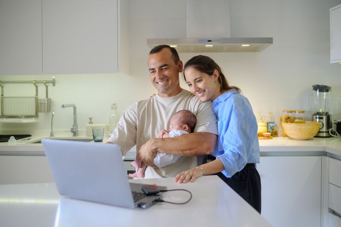 A man and woman holding a baby in front of a laptop