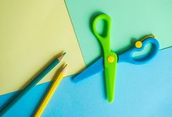 Open blue & green safety scissors and pencils on paper background