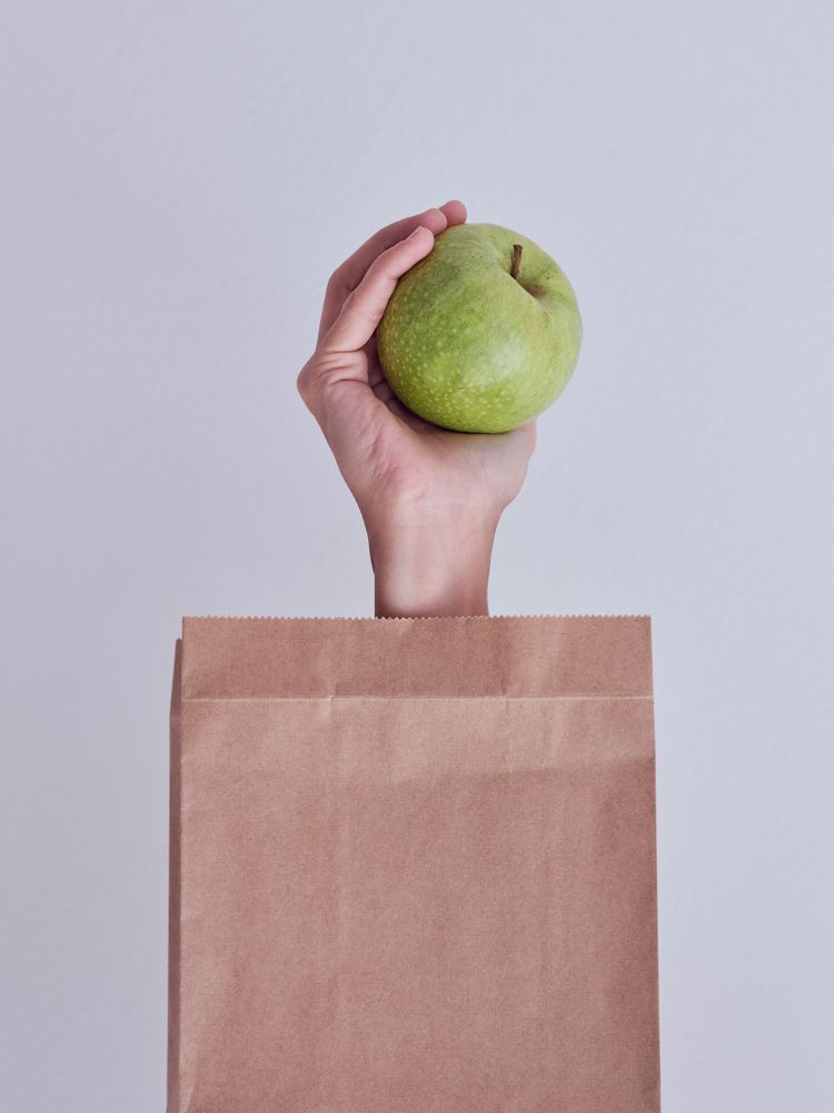 Crop person reached out from paper bag with green apple