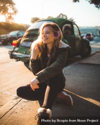 Smiling woman sitting on sidewalk near green beetle car 4A8JR5