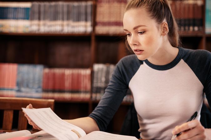 Focused young woman looking for information from textbook