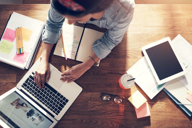 Top view of woman reading on laptop with notebook on wooden desk