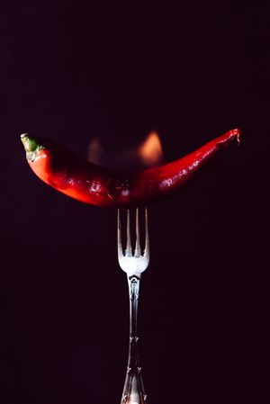 red chili pepper on fire in fork on a dark background